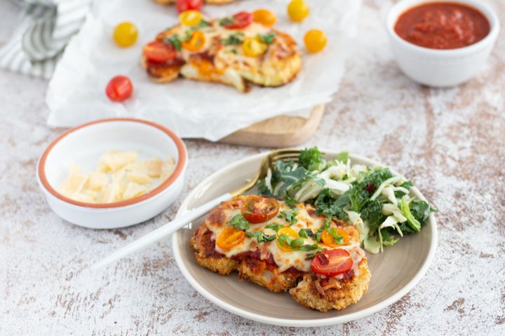 Cauliflower parmesan with breaded cauliflower steaks topped with marinara sauce, melted cheese, and cherry tomatoes.