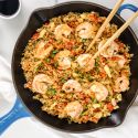 Cauliflower shrimp fried rice with cabbage, carrots, green onions, and soy sauce in a skillet.