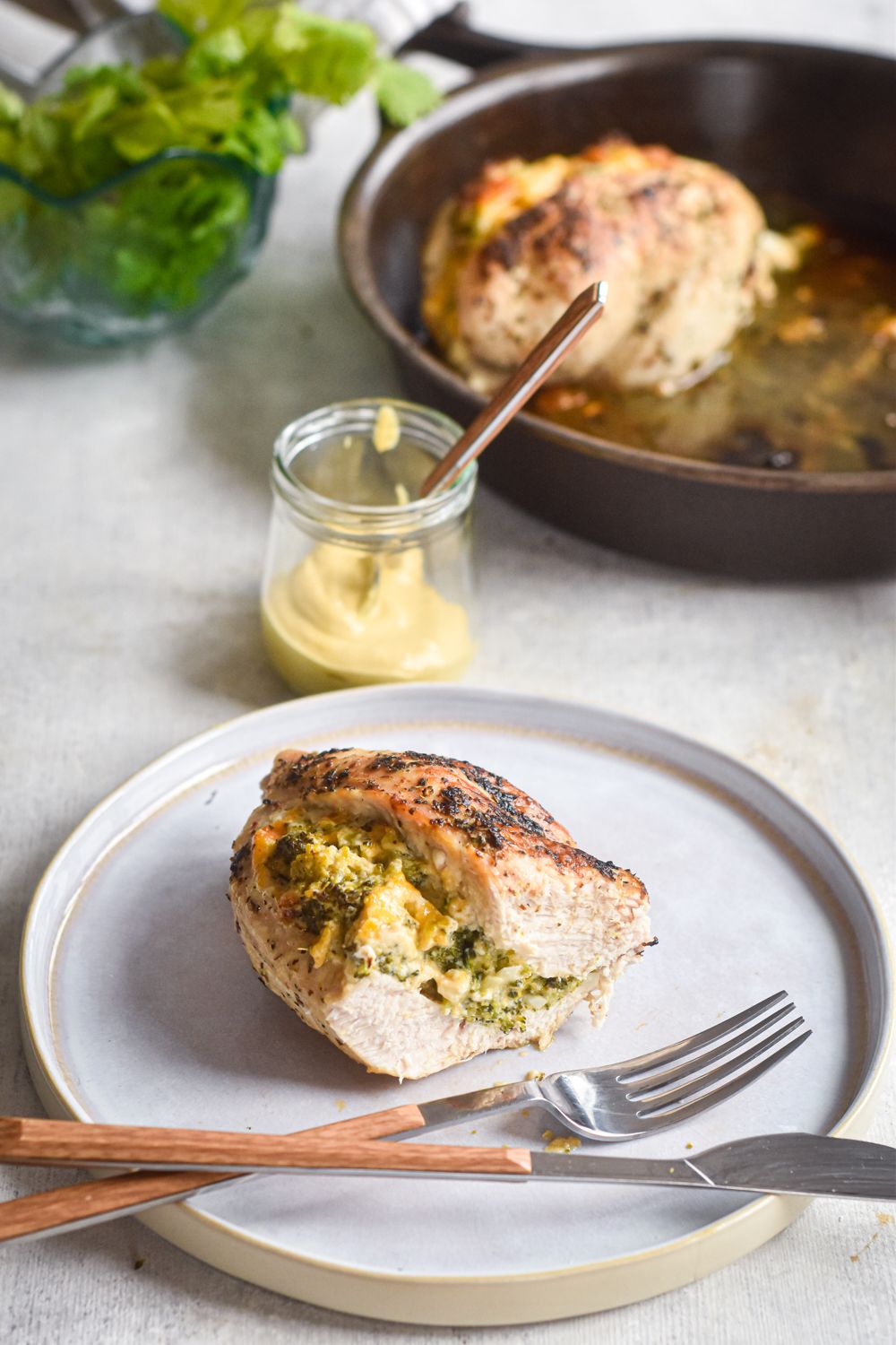 Cheesy broccoli stuffed chicken breasts on a plate with a fork and knife.