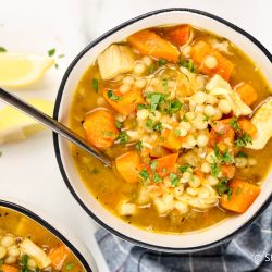 Chicken sweet potato soup with Israeli couscous in a bowl with lemon and parsley.