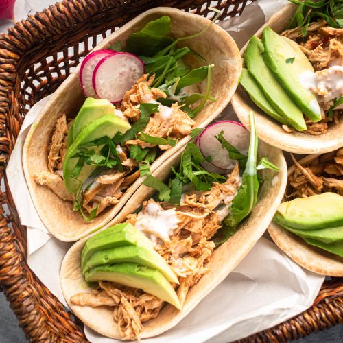 Slow cooker barbacoa chicken shredded and served in corn tortillas with avocado and cilantro.