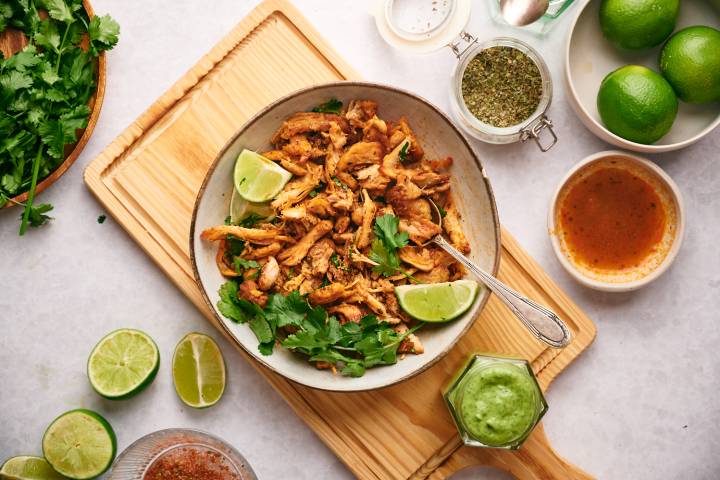 Chicken carnitas made with crispy chicken thighs, spices, and lime juice in a bowl with salsa on the side. 