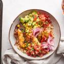 Chicken fajita bowls with seasoned chicken, peppers, onions, corn, and salsa in a bowl with a sheet pan on the side. 