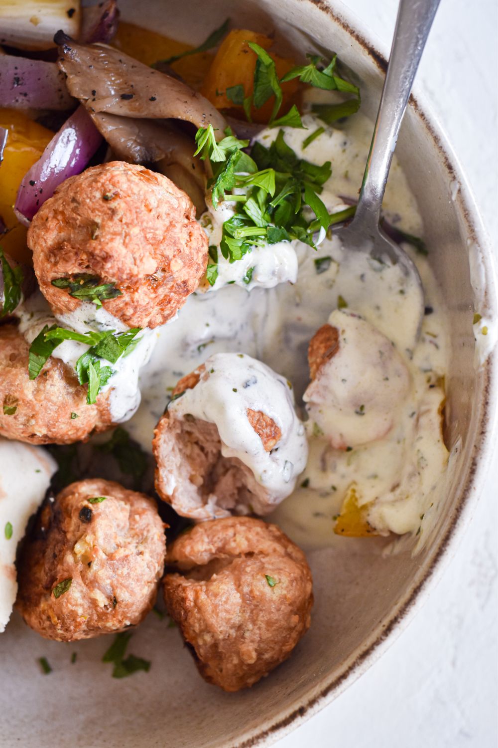 Chicken meatballs made with feta cheese with pita bread, grilled onions, and tzatziki in a bowl.