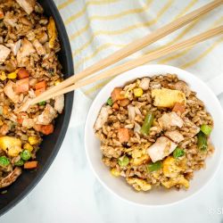 Chicken fried rice in a bowl with eggs, peas, carrots, chicken, and green beans with chopsticks.