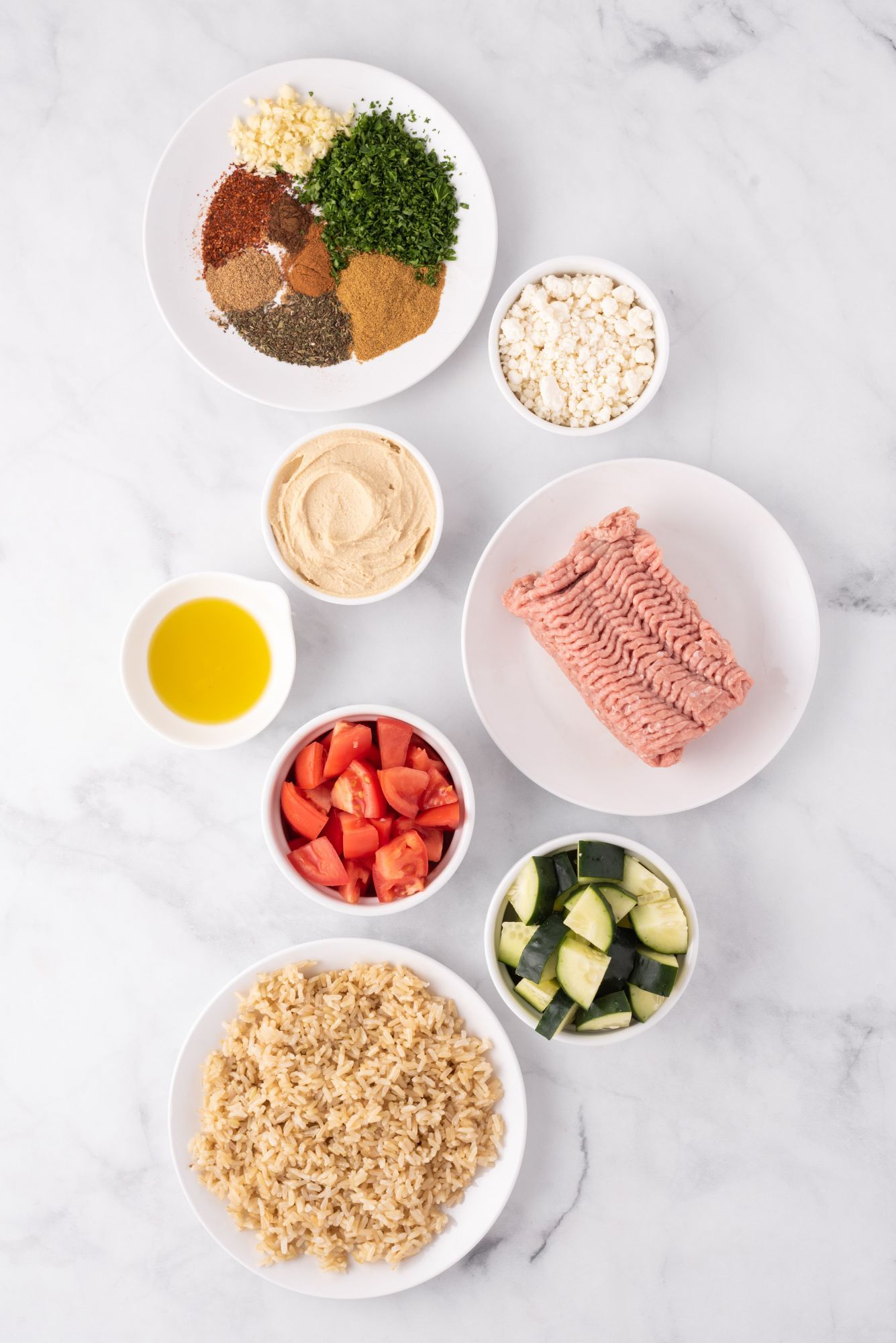 Ingredients for a chicken kofta bowl with ground chicken, Middle Eastern spices, brown rice, cucumbers, and tomatoes.