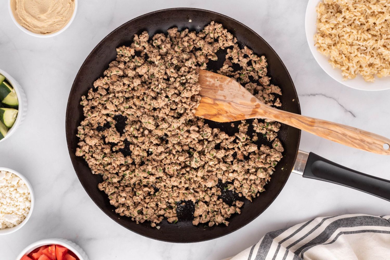 Chicken kofta being cooked in a skillet with spices and a wooden spoon.