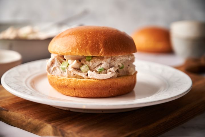 Chicken salad sandwich with shredded chicken, mayonnaise, celery, salt, and pepper on a brioche roll. 