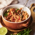 Chicken tinga in a bowl with onions, cilantro, avocado, and queso fresco.