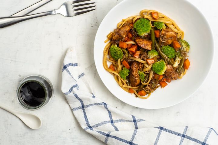 Healthy chicken lo mien with broccoli on a white plate with soy sauce.