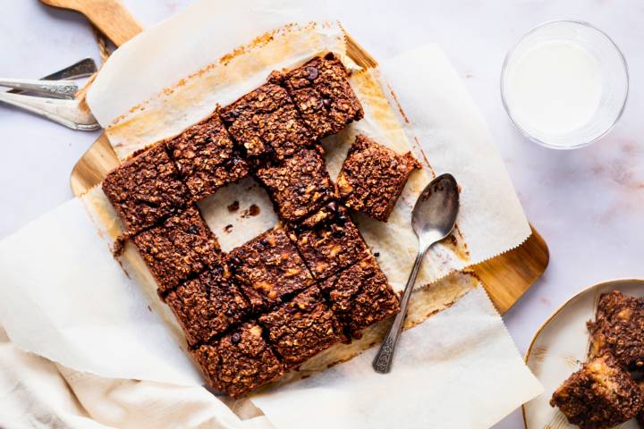 Chocolate baked oatmeal with rolled oats, chocolate chips, banana, and almond milk sliced into squares on a cutting board.