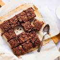 Chocolate baked oatmeal with rolled oats, chocolate chips, banana, and almond milk sliced into squares on a cutting board.