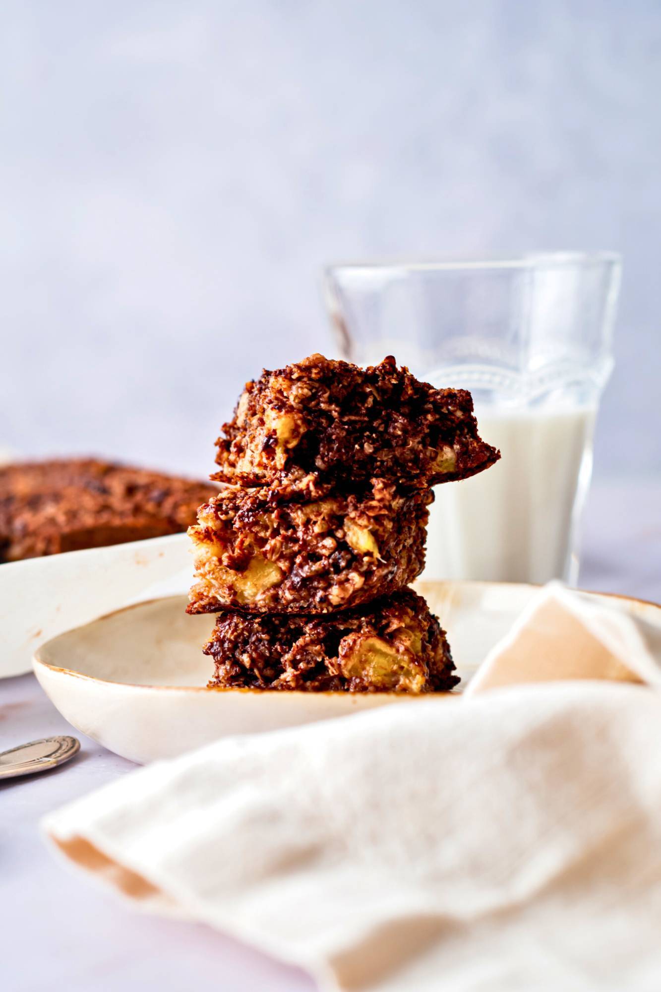 Chocolate baked oats cut into squares and piled on a plate with a glass of milk on the side.