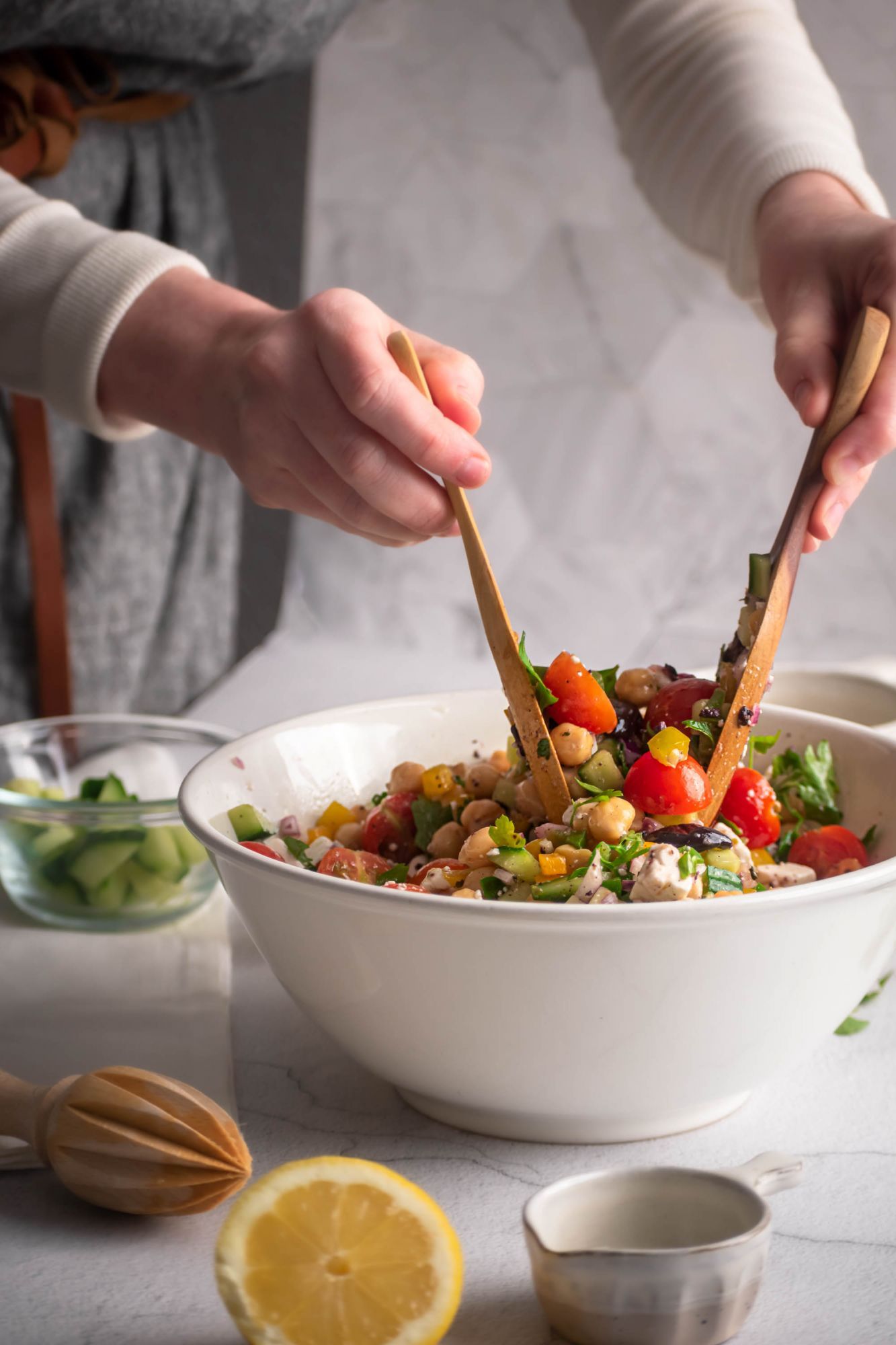 Chopped chickpea salad with Greek ingrdients including feta and Kalamata olives being tossed by two hands.