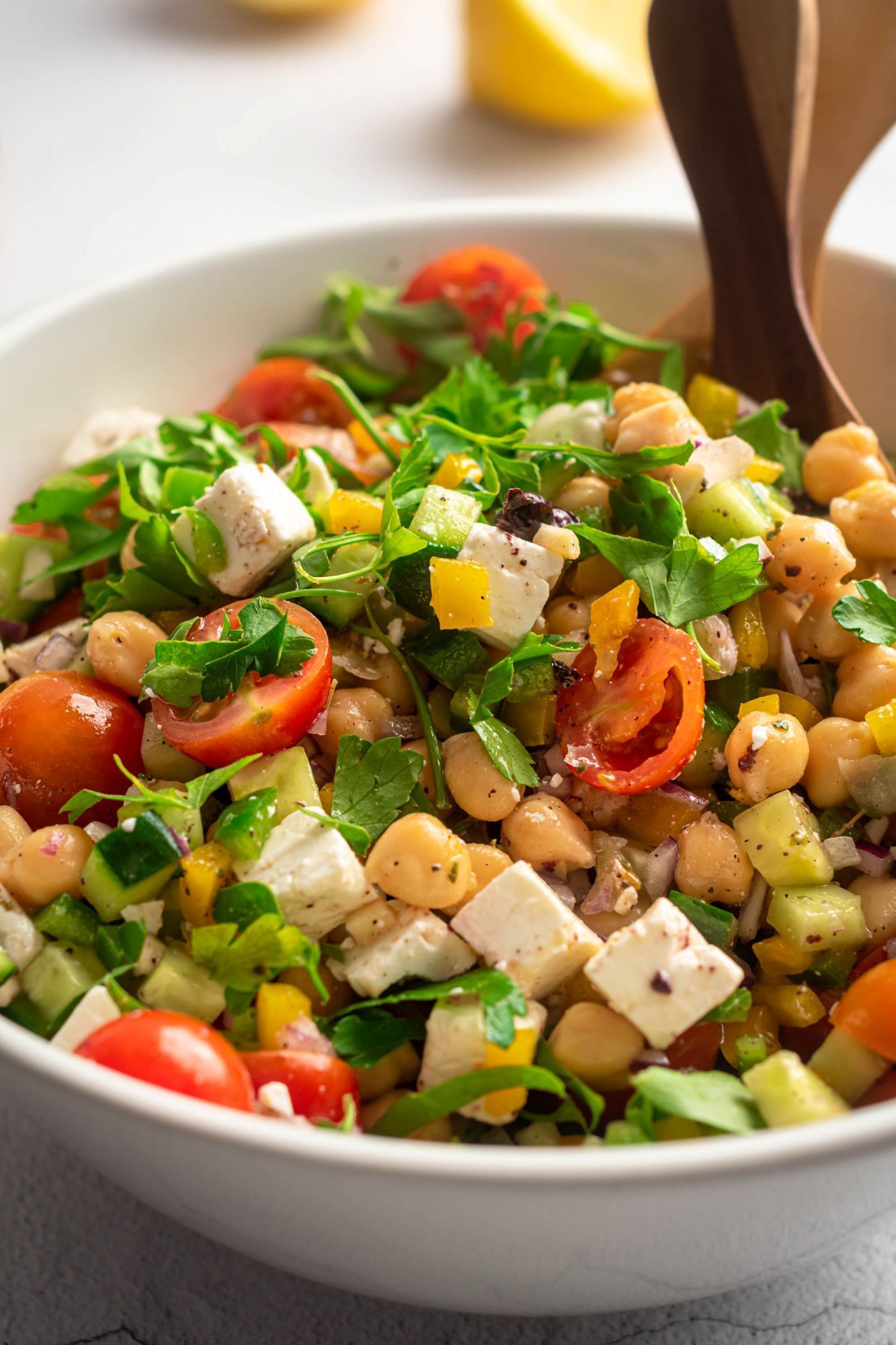 Greek chickpea salad with chopped bell peppers, cucumber, onion, olives, and feta being tossed in a bowl