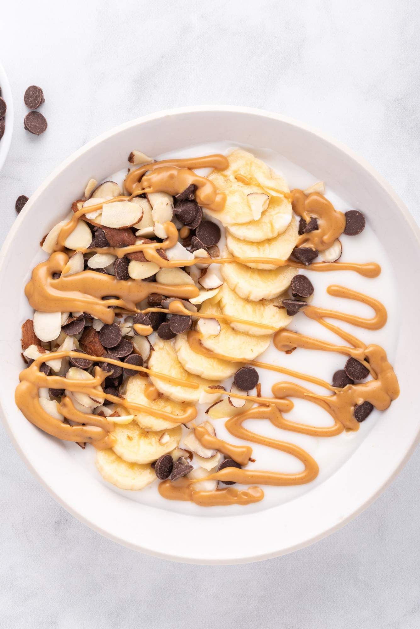 Chunky monkey yogurt bowl with melted peanut butter, bananas, chocolate chips, and almonds.