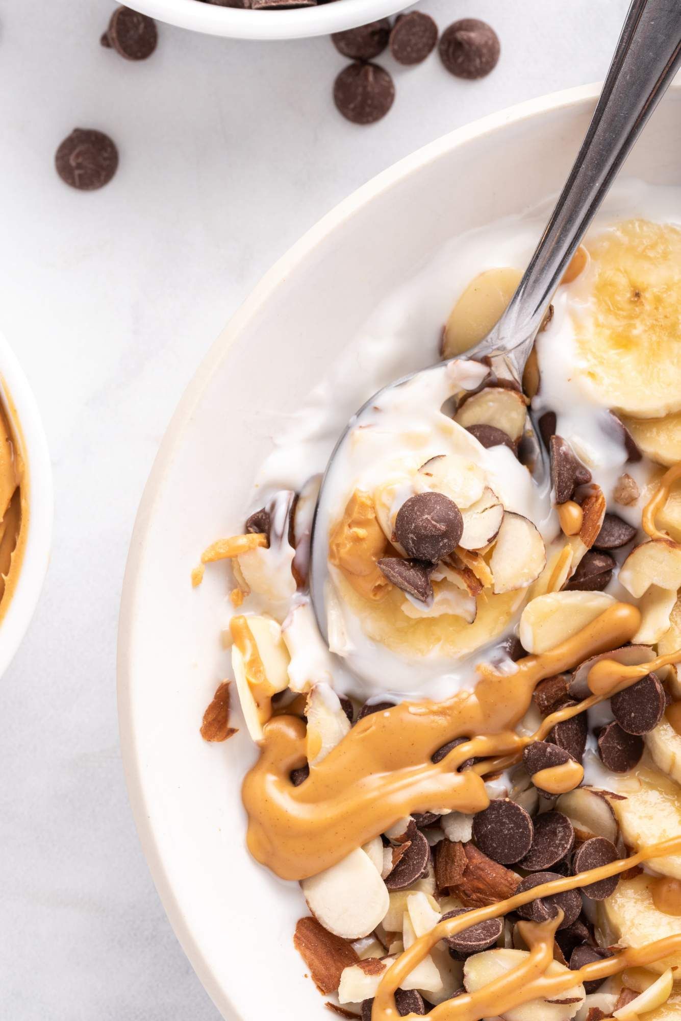 Banana peanut butter Greek yogurt bowl with sliced almonds and chocolate chips in a bowl with a spoon.