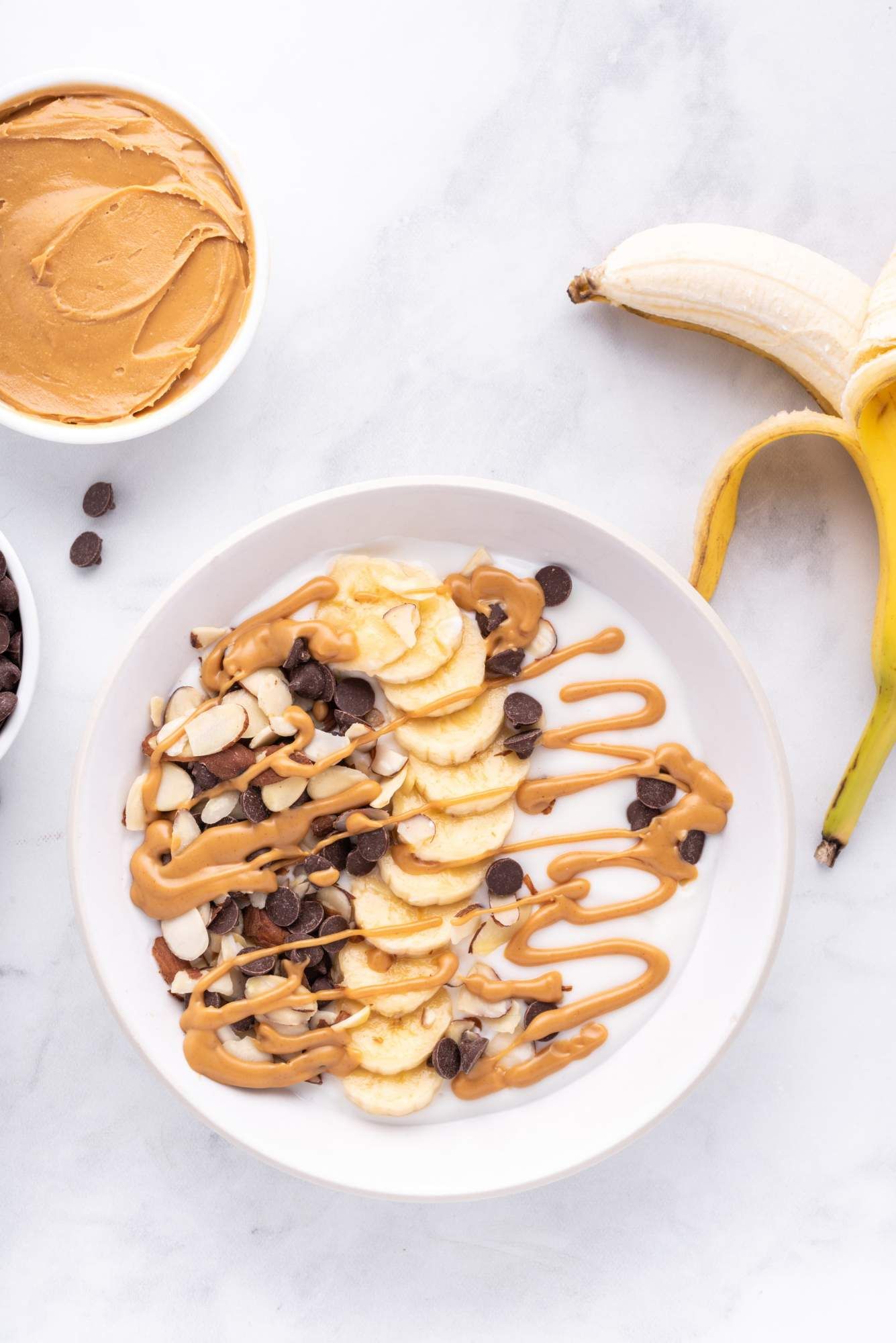 Greek yogurt bowl with sliced bananas, chocolate chips, sliced almonds, and melted peanut butter drizzled on top.