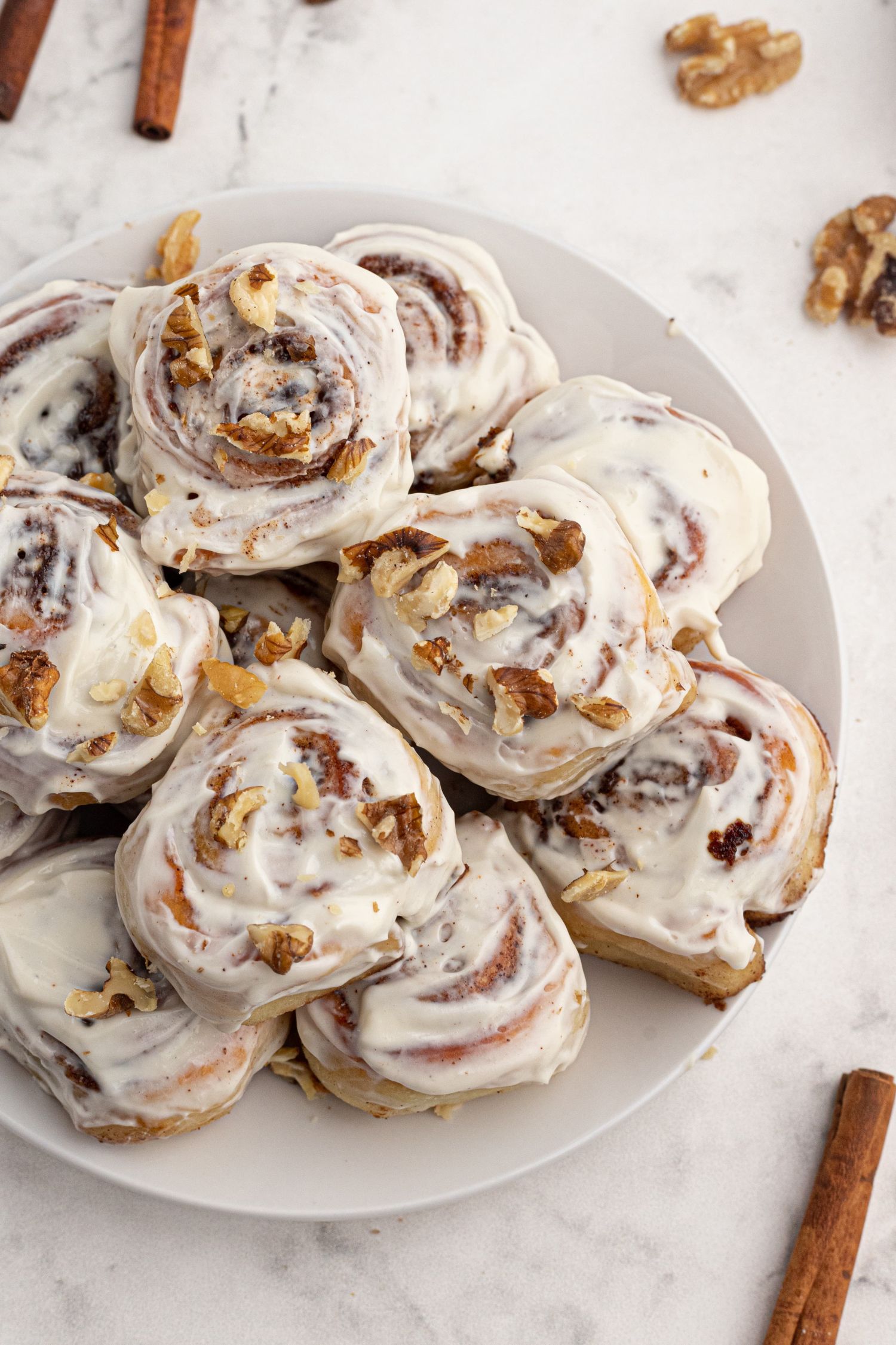 Plate fo homemade cinnamon rolls with cream cheese icing, walnuts, and cinnamon.