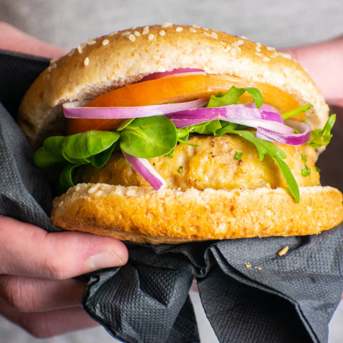 Turkey burgers with lettuce, tomatoes, red onions, cheese, and sprouts on a wheat bun.