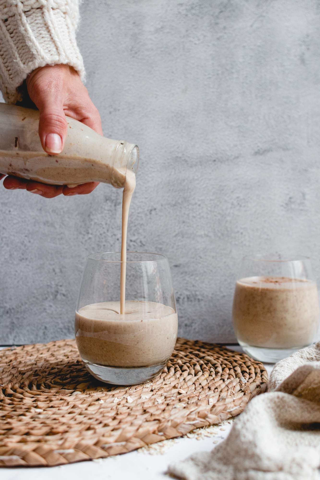 Banana oatmeal smoothie being poured into a glass with blended oats, banana, cinnamon, maple syrup, and almond butter.