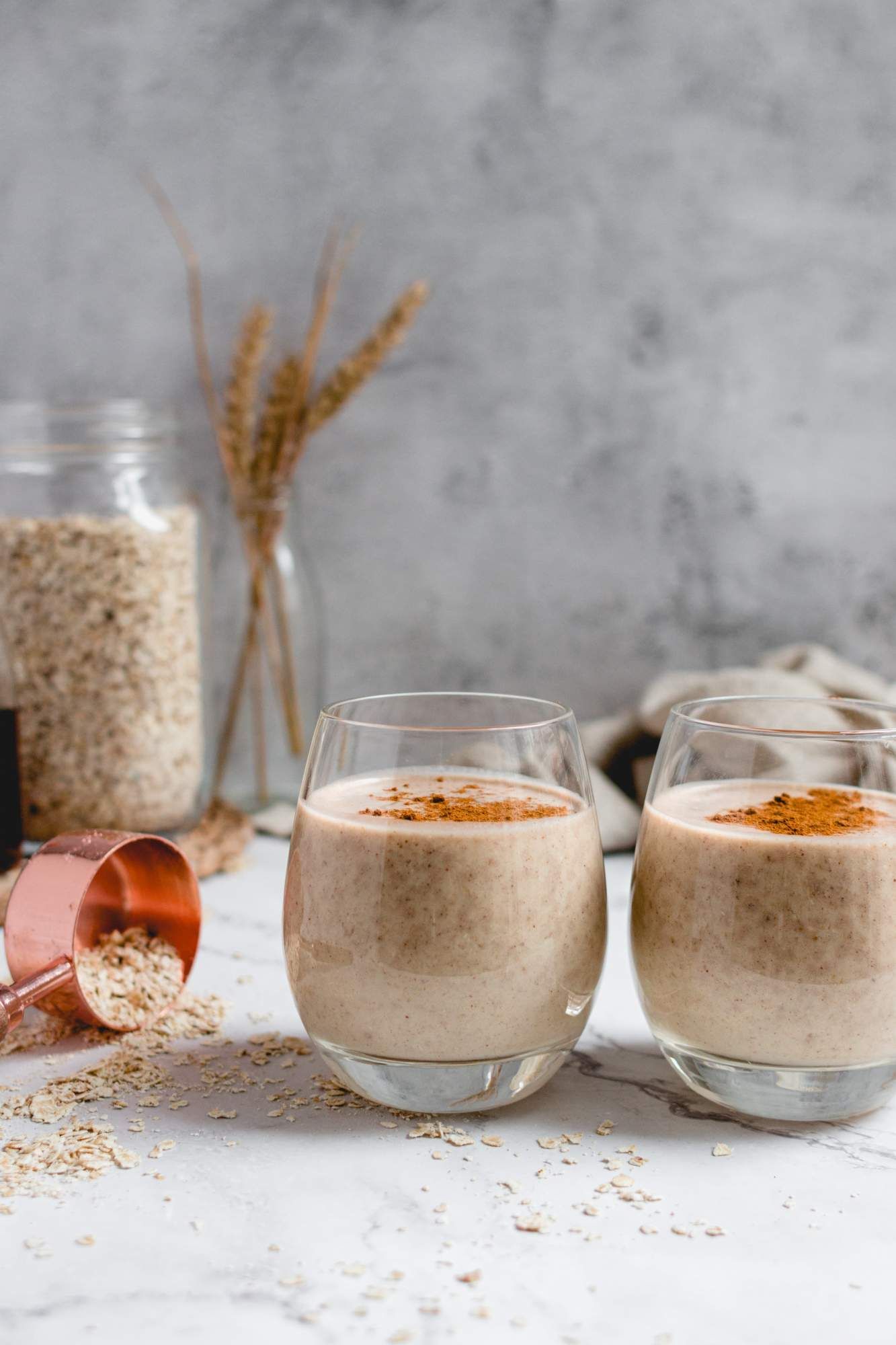 Two oatmeal banana smoothies in glasses with loose oats on the side.