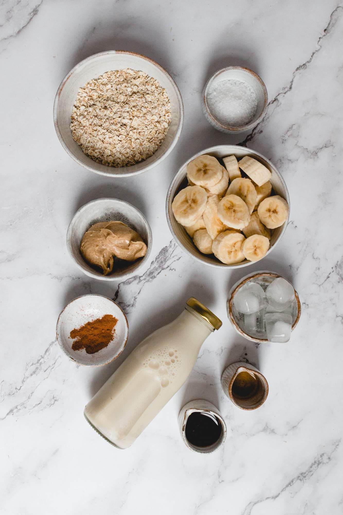 Ingredients to make a banana oatmeal smoothie including bananas, rolled oats, cinnamon, almond butter, and almond milk.