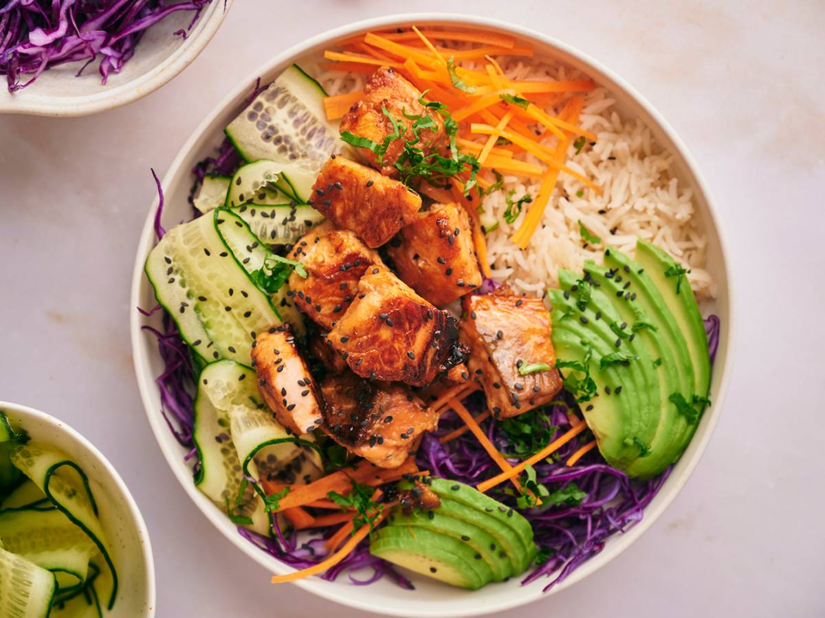 Salmon rice bowl with salmon pieces that are crispy served with rice, purple cabbage, edamame, carrots, and cucumber.