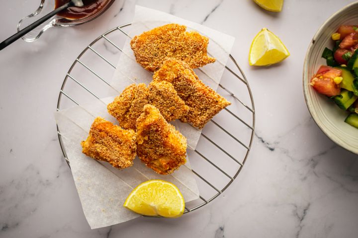 Crispy baked fish with breading on a wire rack with lemons and salad.