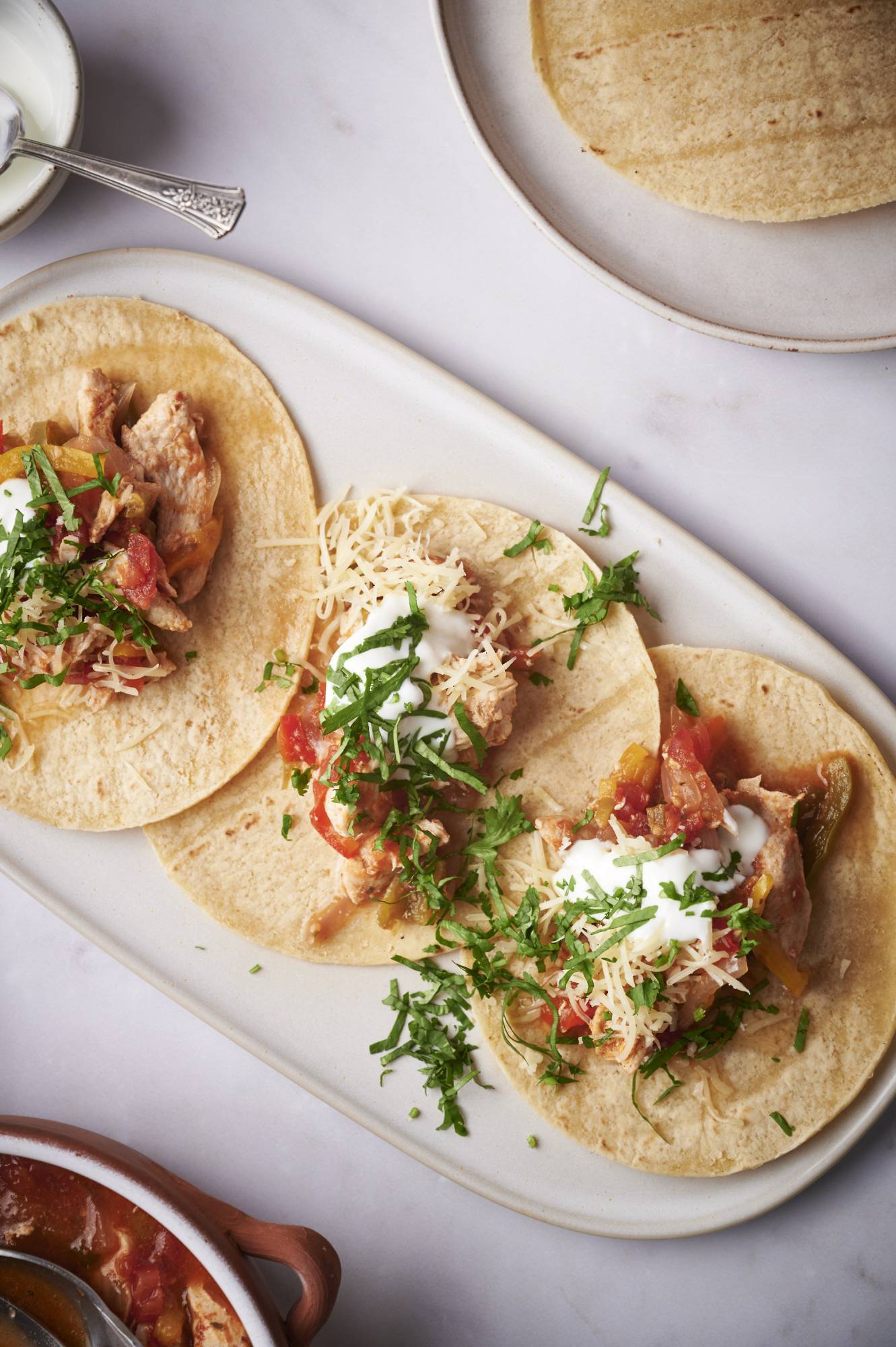 Chicken fajitas served on corn tortillas with sour cream, cilantro, and shredded cheese.