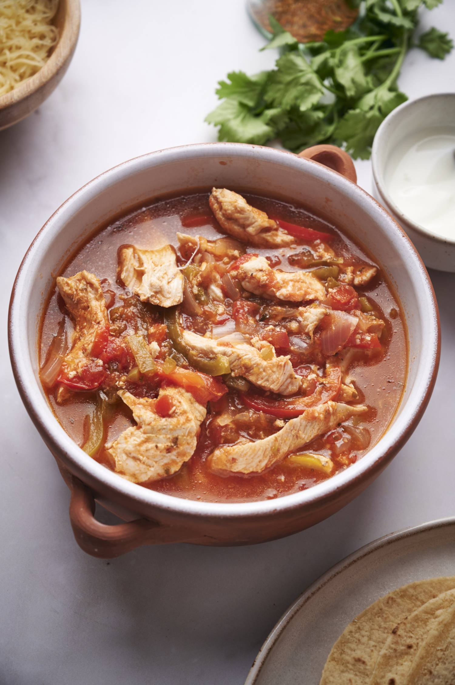 Slow cooker chicken fajitas served in a bowl with tortillas, cheese, and cilantro on the side.