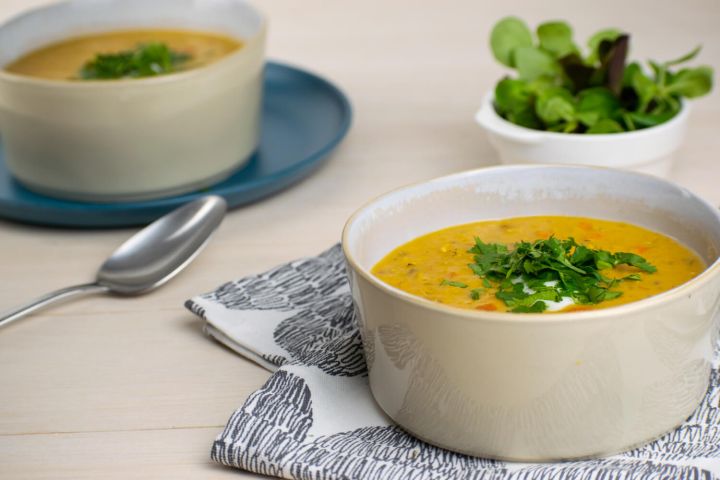 Slow cooker red lentil soup with curry powder and carrots in a bowl with herbs and yogurt.