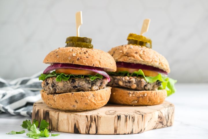 Double bean burgers made with black beans, white beans, cilantro, onion, and spices cooked and served on wheat buns with vegetables.