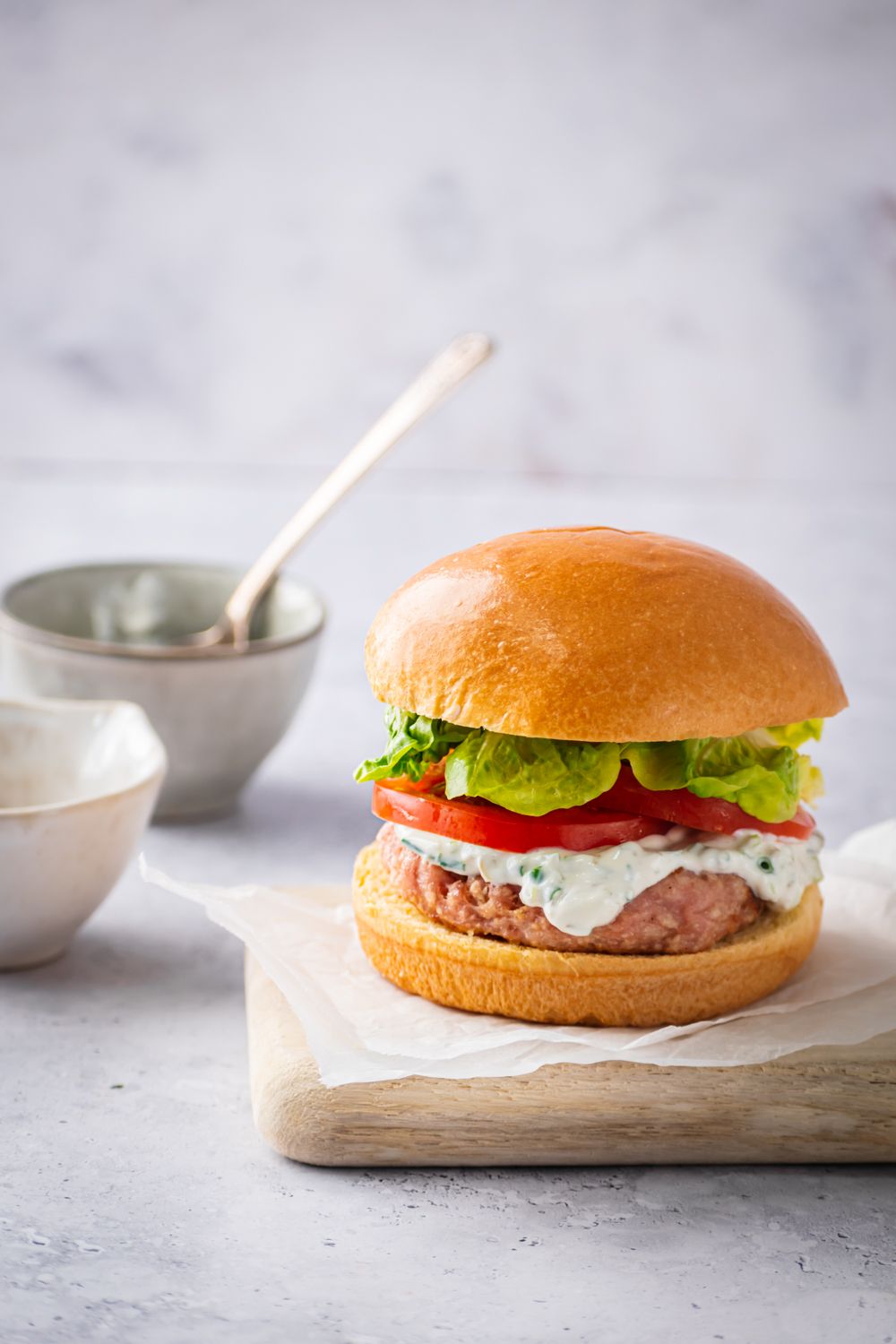 Easy chicken burgers with ground chicken patties topped with yogurt sauce, tomatoes, and lettuce on a bun.