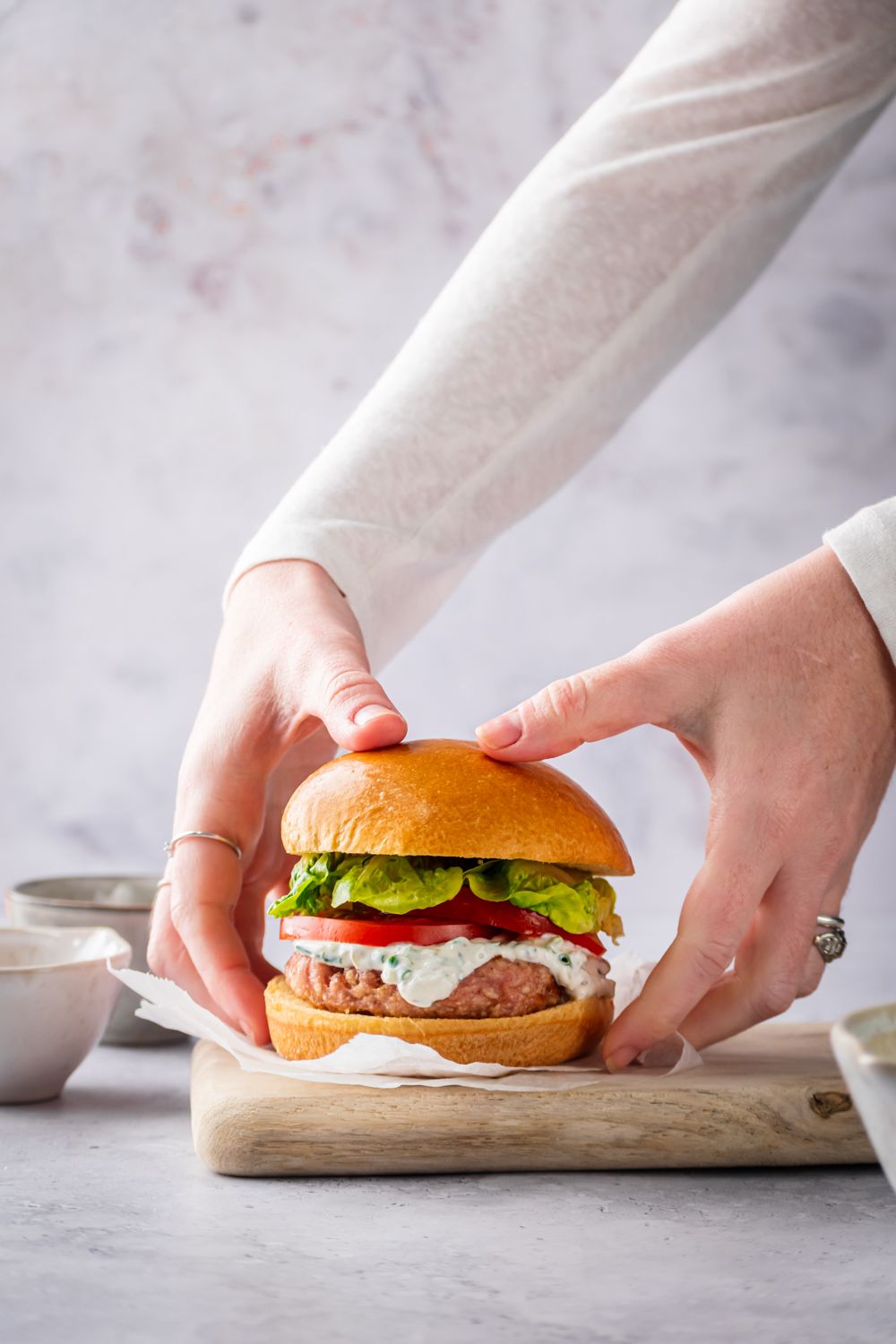 Chicken burgers made with ground chicken and seasoning on a bun being picked up by two hands.