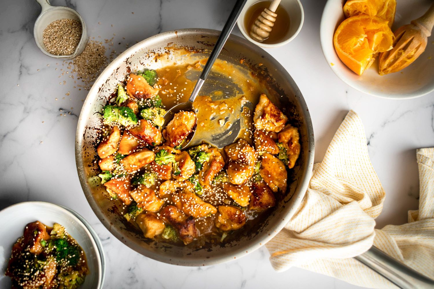 Easy orange chicken with broccoli served in a skillet with sticky sauce and sesame seeds.