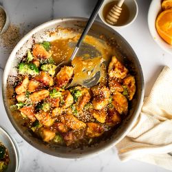 Easy orange chicken with broccoli served in a skillet with sticky sauce and sesame seeds.