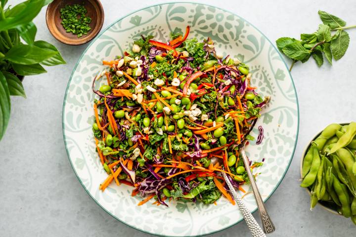 Edamame salad with shelled edamame, kale, carrots, red bell peppers, peanuts, cilantro, and mint served with peanut dressing.