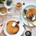 Low carb Flaxseed meal pancakes stacked on a plate with berries, yogurt, and a drizzle of syrup.