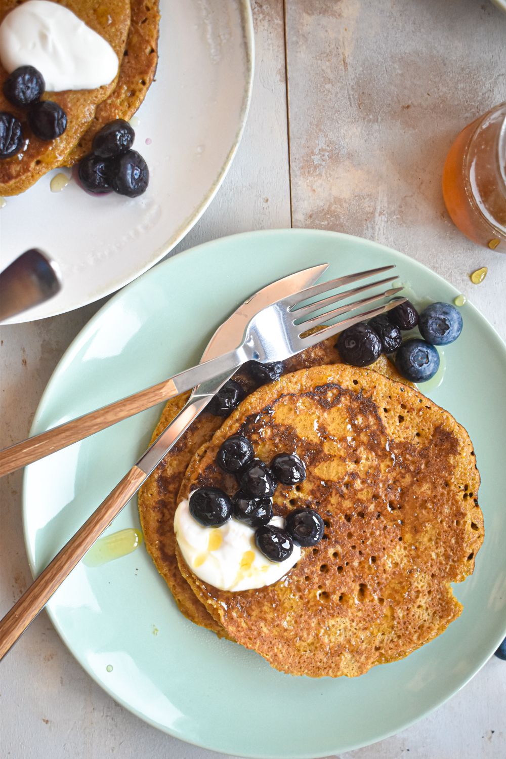 Flax pancakes with yogurt and blueberries on a plate with a fork and knife.