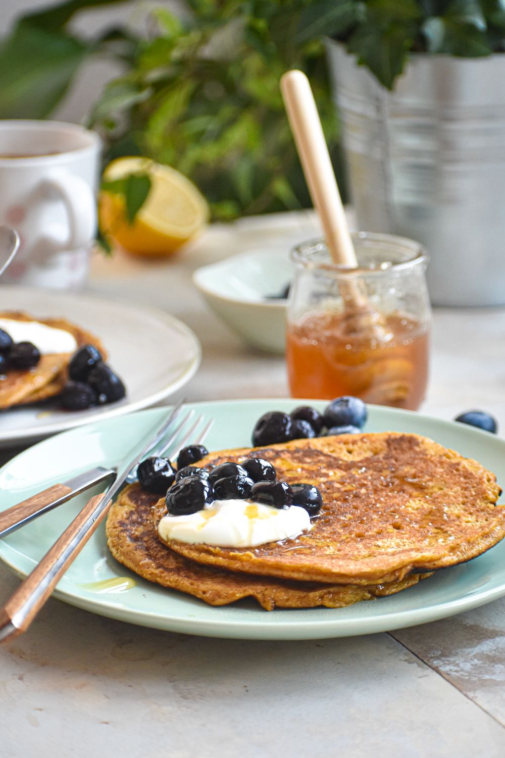 Low carb flax pancakes on a plate with yogurt, berries, and syrup with lemon on the side.