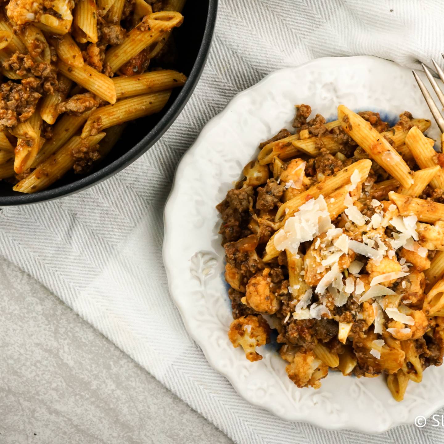 Sausage pasta with cauliflower, garlic, and tomatoes on a plate with Parmesan cheese.