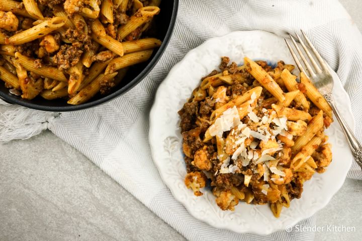 Sausage pasta with cauliflower, garlic, and tomatoes on a plate with Parmesan cheese.