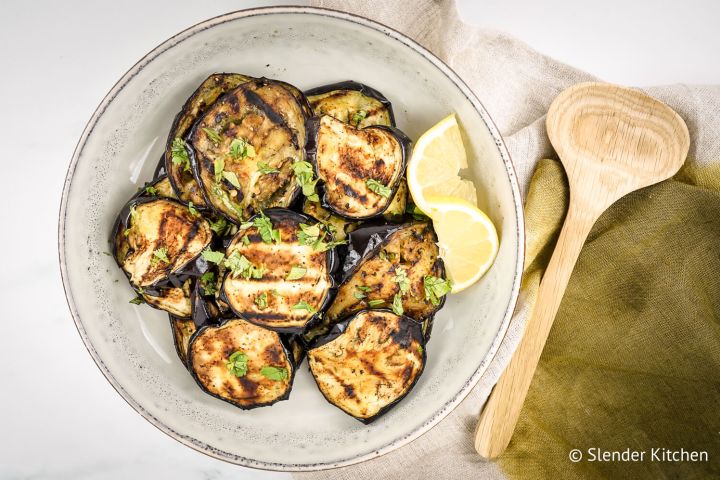 Grilled eggpplant with garlic, lemon, and parsley on a ceramic plate.