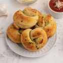 Garlic knots made with two ingredient dough topped with fresh garlic, melted butter, and basil on a plate with marinara sauce on the side.