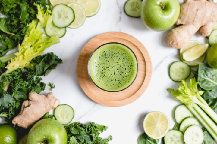 Green juice made with cucumbers, celery, kale, spinach, green apples, ginger, and lime juice in a glass.