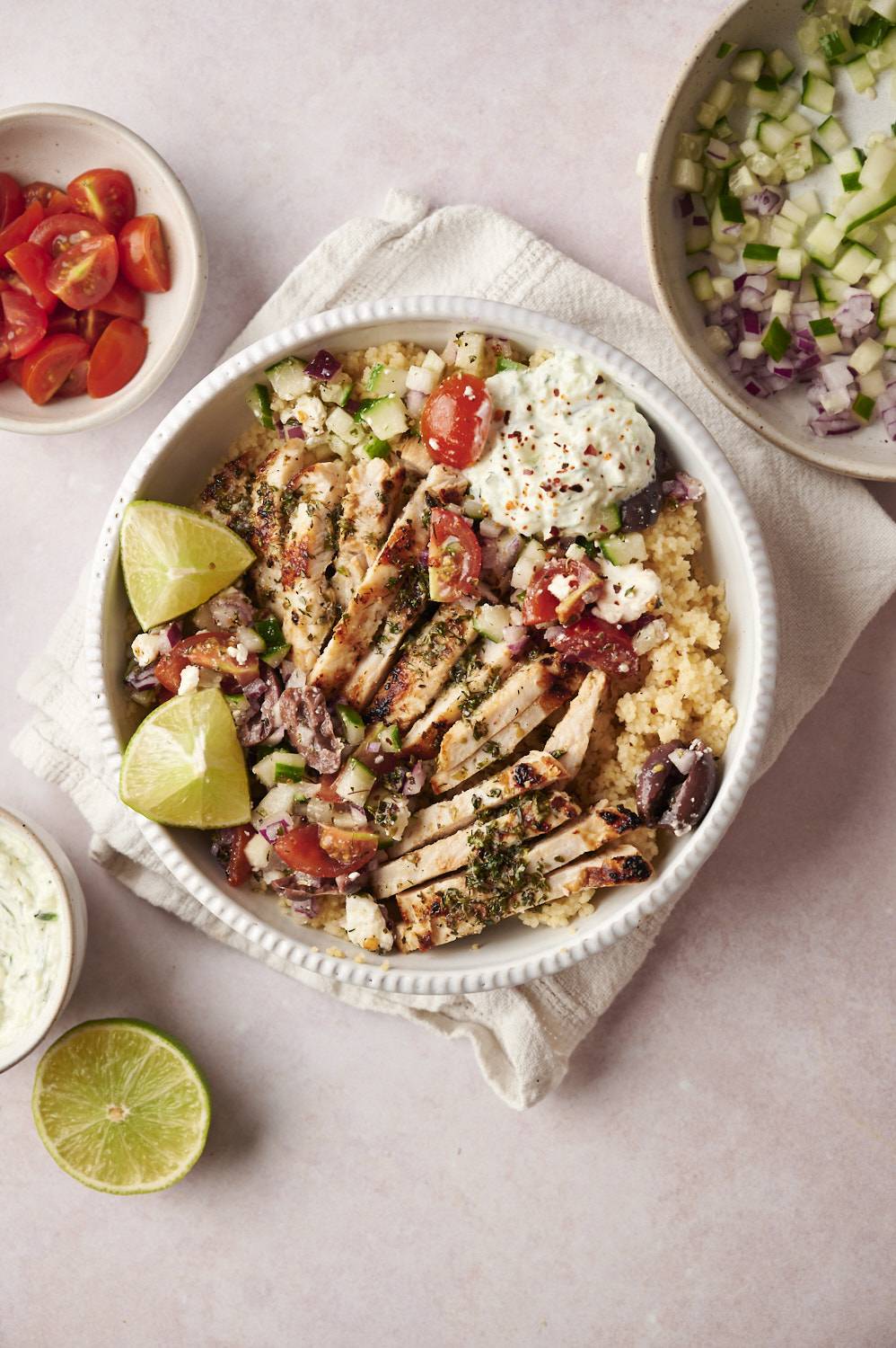 Greek chicken quinoa bowls with feta cheese, black olives, tzatziki, and Greek salad in a bowl.