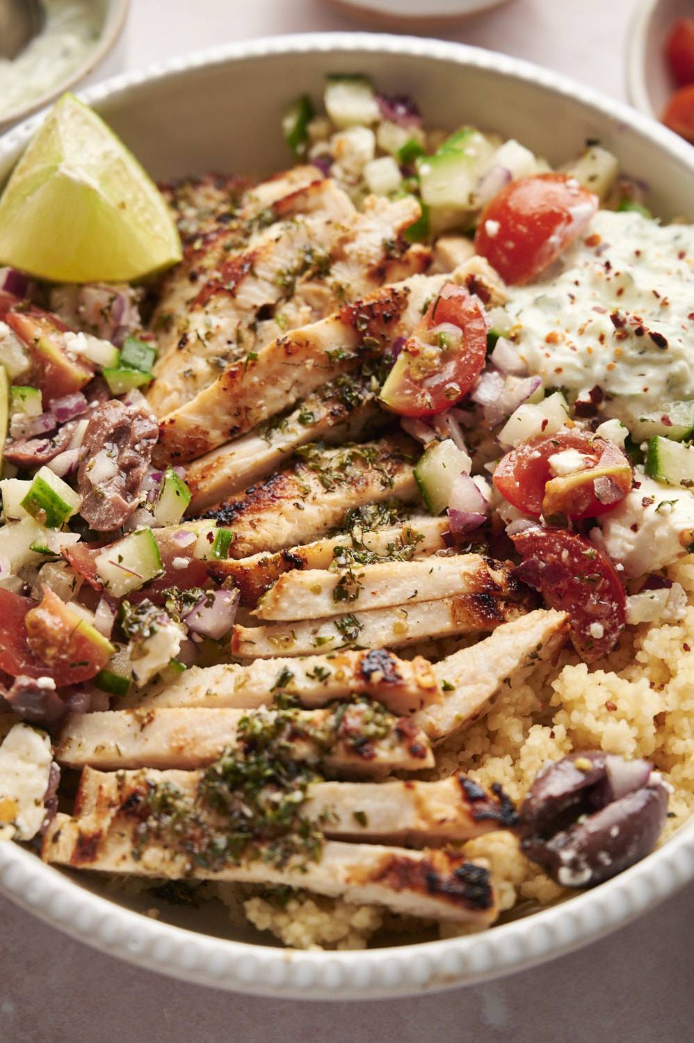 Greek chicken breast bowls with quinoa, feta cheese, salad, tzatziki, and oregano in bowl.