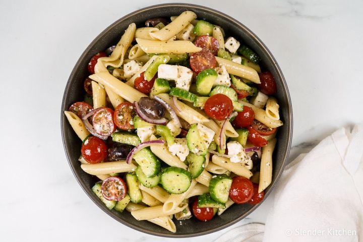 Greek pasta salad with tomatoes, cucumbers, black olives, feta cheese, and Greek dressing in a bowl. 