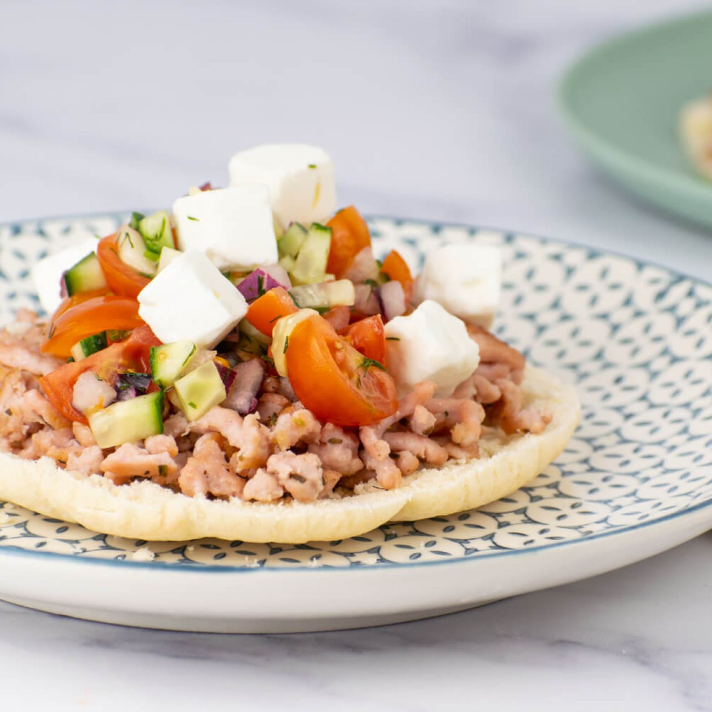 Greek turkey tostadas with tomatoes, cucumbers, and feta cheese on toasted pita bread.